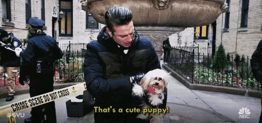 a man is holding a small white dog and saying that 's a cute puppy .