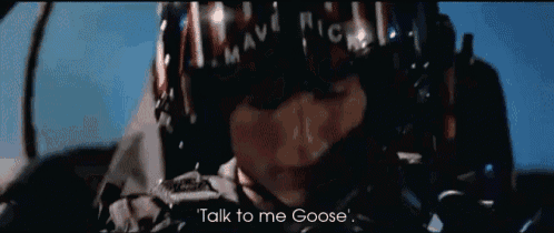 a man in a helmet is talking on a cell phone and says talk to me goose .