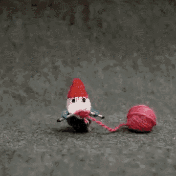 a crocheted gnome is playing with a ball of yarn on the ground .