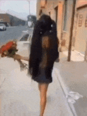 a woman is walking down the street with a bouquet of flowers in her hand .