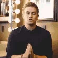 a young man is sitting in front of a mirror with his eyes closed and his hands folded in prayer .