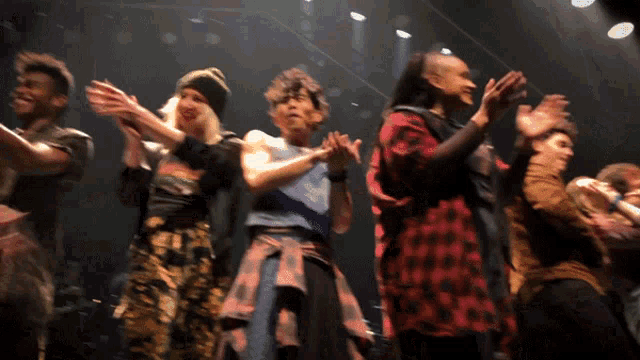 a group of people are dancing on a stage with their hands up