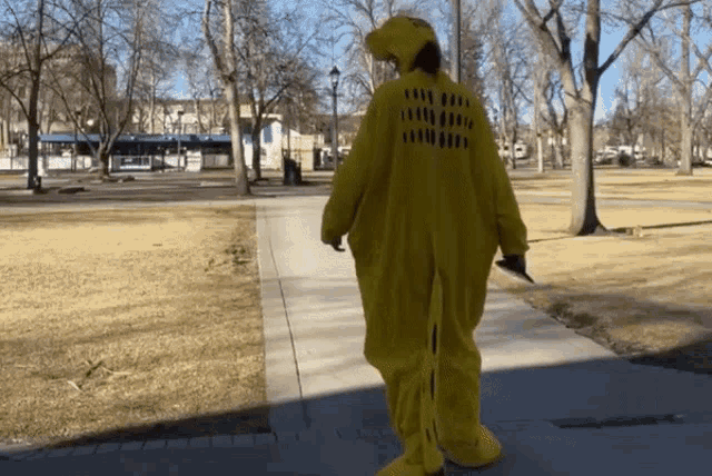 a person in a yellow dinosaur costume is walking down the sidewalk