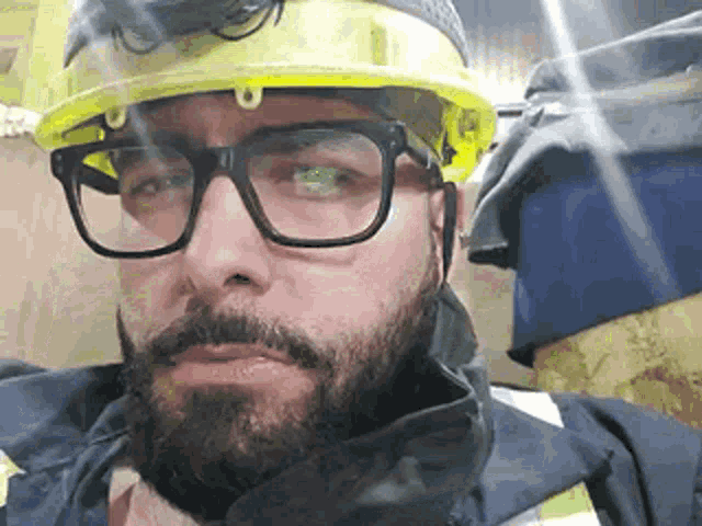 a man with a beard and glasses is wearing a hard hat and safety glasses .