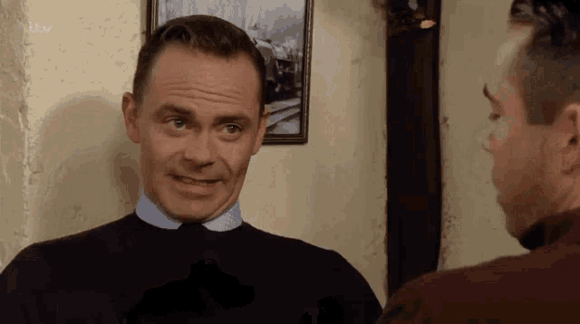 two men are standing next to each other in a room talking to each other .