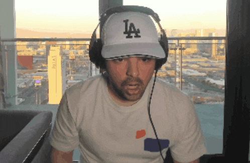 a man wearing a la hat and headphones looks at the camera