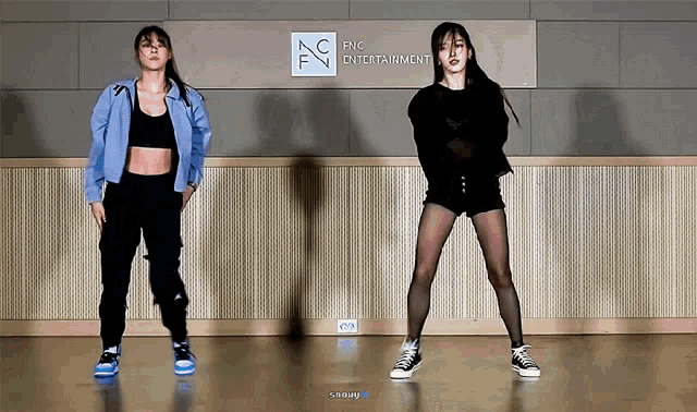 two girls are dancing in front of a sign that says fnc entertainment