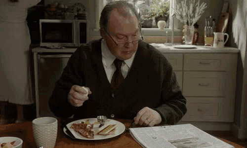 an elderly man sitting at a table eating bacon and toast