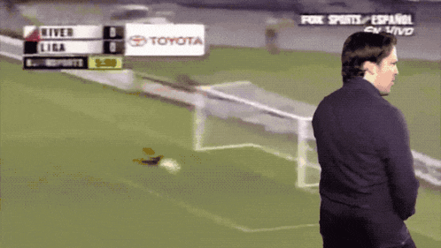 a man stands on a soccer field in front of a scoreboard that says toyota