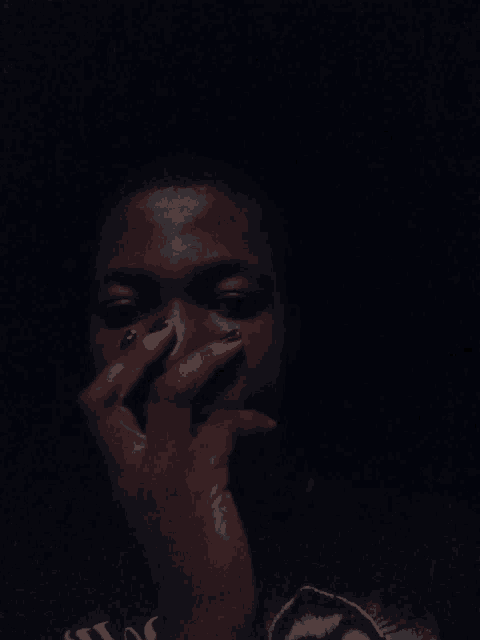 a close up of a person covering their face with their hand in the dark