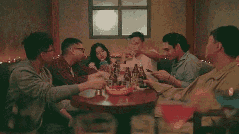 a group of people are sitting around a table toasting with glasses of beer .