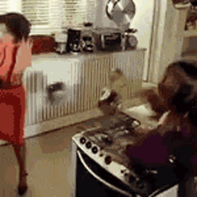 a woman in a red dress is standing next to a stove in a kitchen