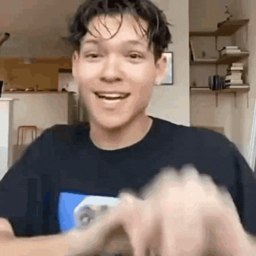 a young man in a black t-shirt is smiling while holding a video game controller .