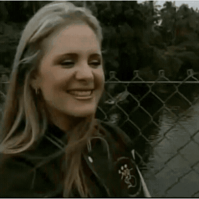 a woman is standing in front of a chain link fence and smiling