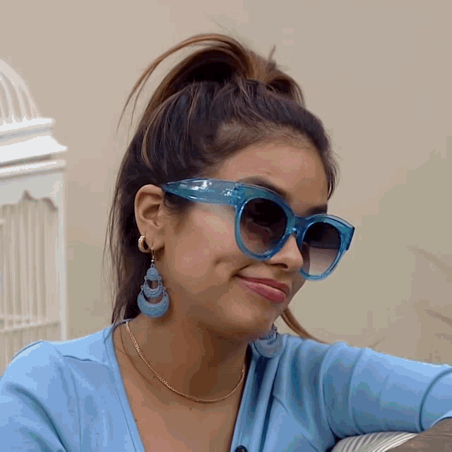 a woman wearing a ponytail and sunglasses looks at the camera
