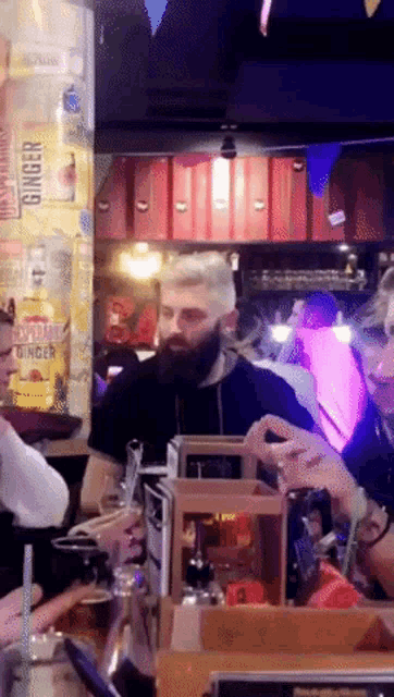 a man with a beard sits at a table in front of a display of ginger beer