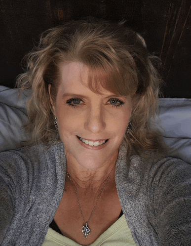 a woman wearing a gray sweater and a necklace smiles for the camera