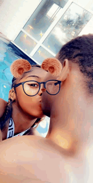 a man and a woman wearing glasses are kissing by a pool