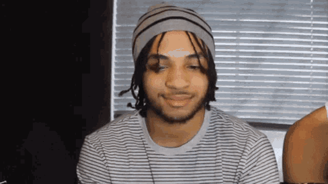 a young man wearing a beanie and a striped shirt looks at the camera