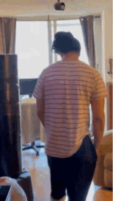 a man is standing in a living room wearing a striped shirt and black pants .