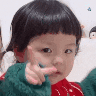a little girl is pointing at the camera while wearing a green sweater and a red sweater .