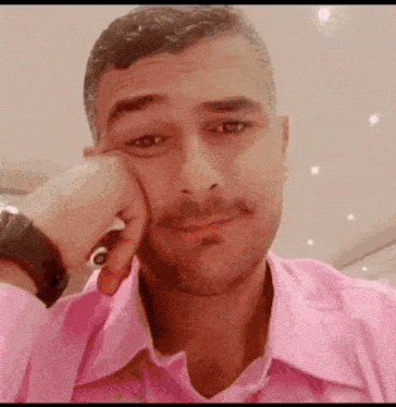 a man in a pink shirt is holding his hand to his face and smiling .