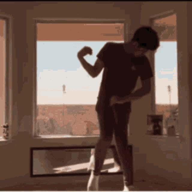 a man in a red shirt flexes his muscles in front of a window
