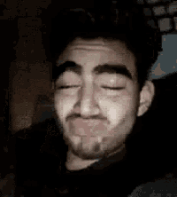 a man with a beard is crying with his eyes closed and his hand on his head .