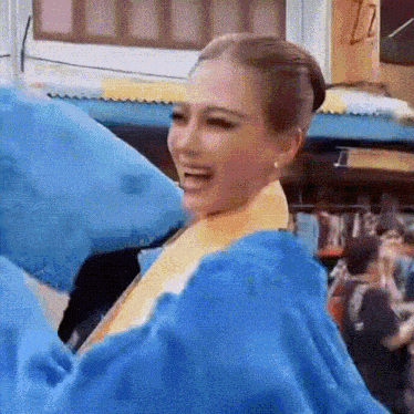 a woman wearing a yellow top and a blue jacket is smiling