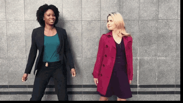 two women standing next to each other with one wearing a pink trench coat