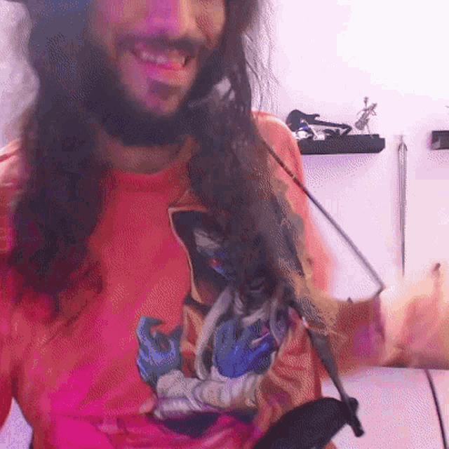 a man with long hair and a beard is wearing a pink shirt with a picture of a woman on it