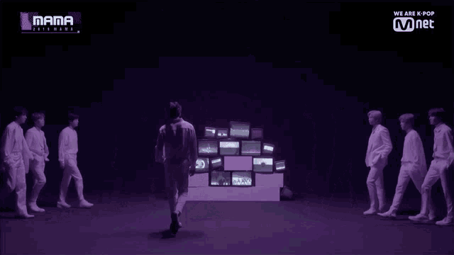 a group of people are walking in front of a wall of televisions with the words mama on the bottom