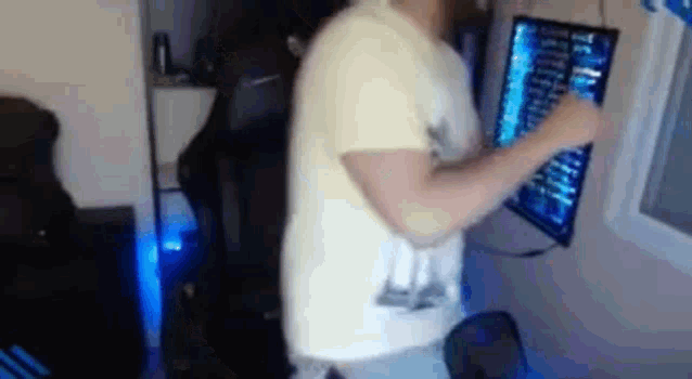 a man in a yellow shirt is standing in front of a computer monitor .