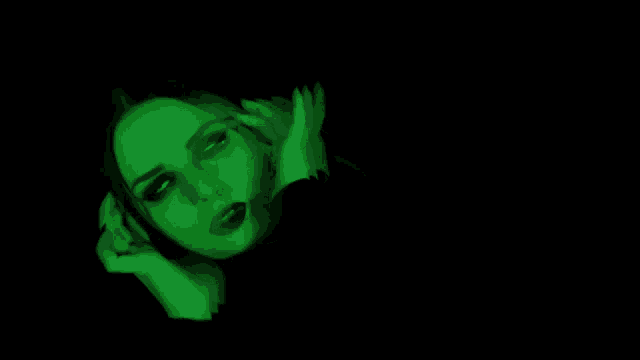 a woman 's face is glowing green in a dark room