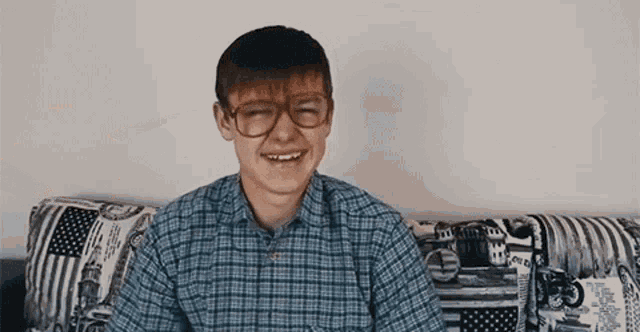 a young man is sitting on a couch wearing glasses and a plaid shirt .
