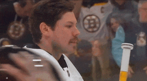 a hockey player is sitting on the ice with a beer in his hand and looking at the camera .