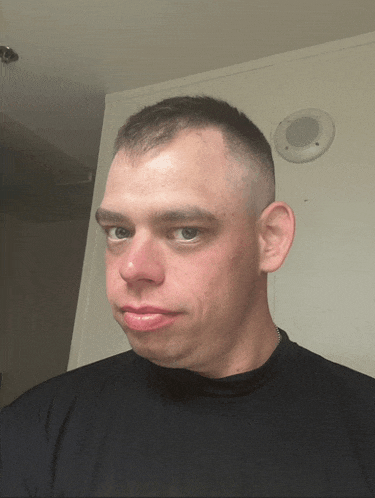 a man with a shaved head looks at the camera in front of a white wall