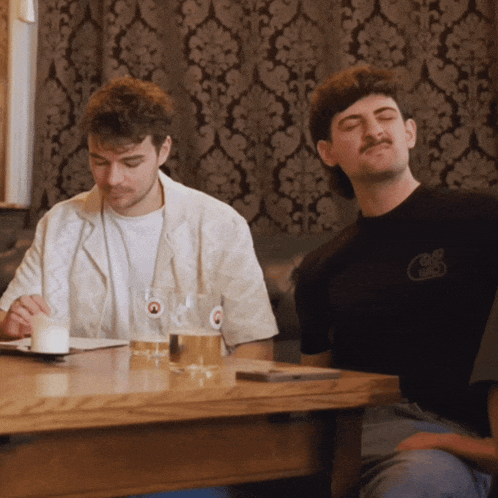 two men are sitting at a table with one wearing a shirt that says ' club chaos '