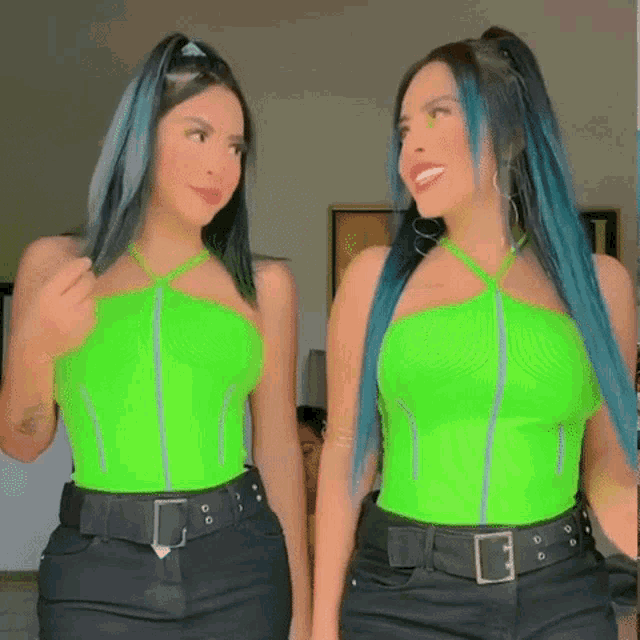 two women are standing next to each other wearing green tops and black skirts .