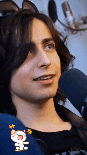 a young man with long hair is sitting in front of a microphone and wearing a cat ear headset .
