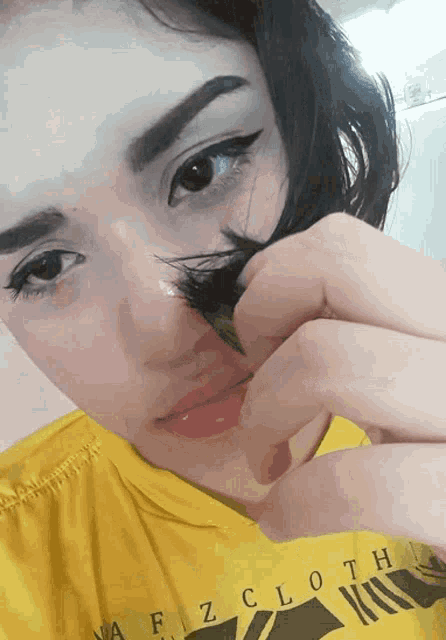 a woman wearing a yellow shirt with the word cloth on it holds her hair