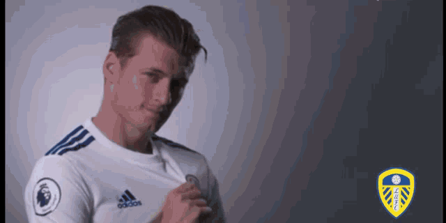 a man in a white adidas shirt is standing in front of a gray background