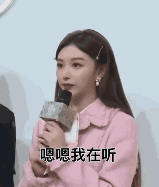 a woman in a pink coat is holding a microphone in her hand .