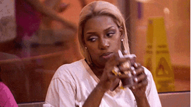 a woman is sitting at a table holding a drink in her hand and looking at her phone .
