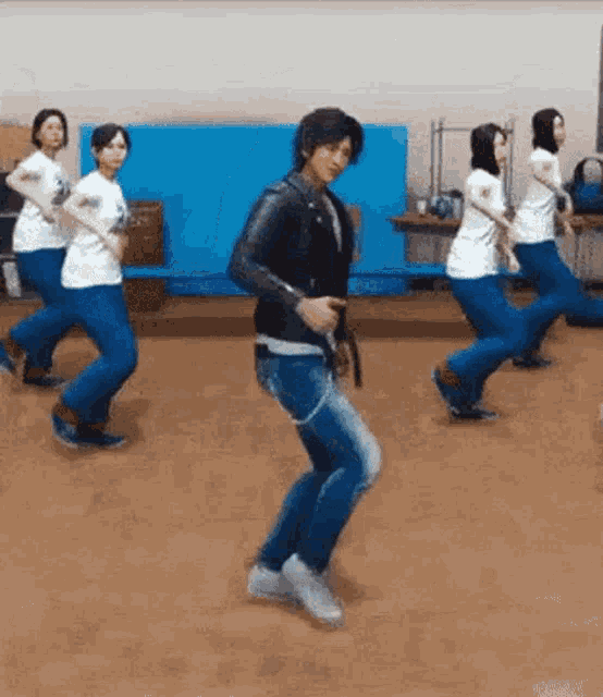 a man in a leather jacket is dancing with a group of women in a gym .