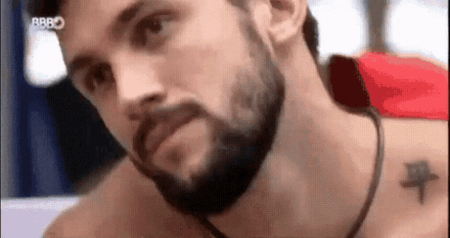 a man with a beard and a tattoo on his chest is laying down .