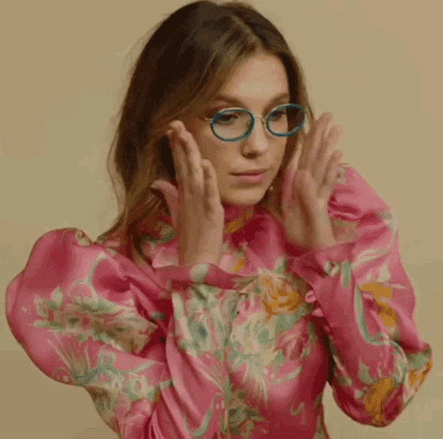 a woman wearing glasses and a pink shirt is making a funny face .
