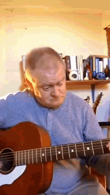 a man is playing an acoustic guitar in front of a bookshelf