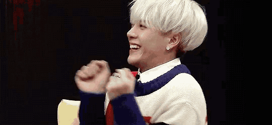 a young man with white hair is laughing and holding his hands up in the air .