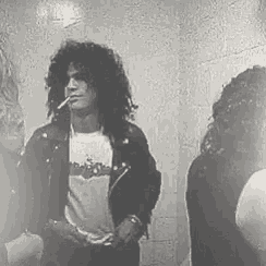 a man with curly hair is smoking a cigarette while standing next to two women .